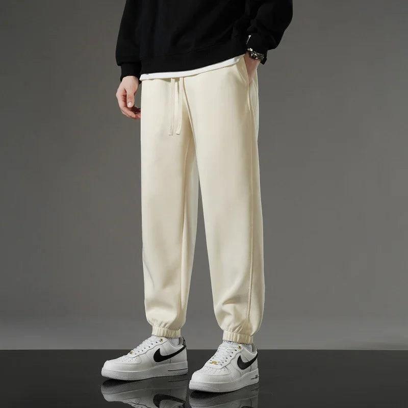 Cream drawstring joggers with elastic cuffs, styled with white sneakers for casual comfort wear.