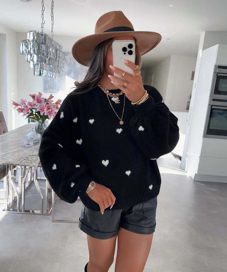 Woman in black heart-print sweater, leather shorts, and wide-brim hat for stylish comfort wear
